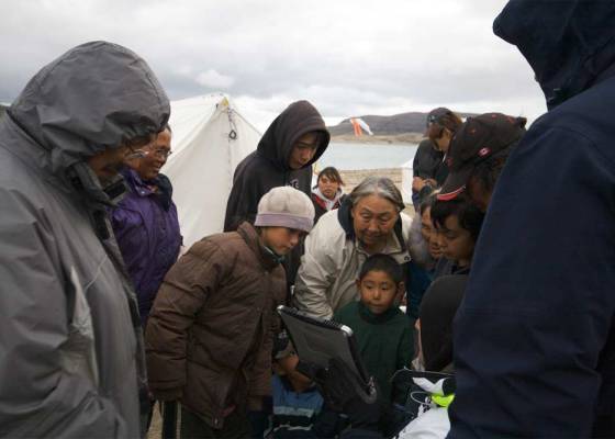 A group of Inuit people gather around a portable device