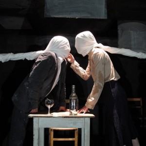 Two people, faces covered by sheets, face each other over a table