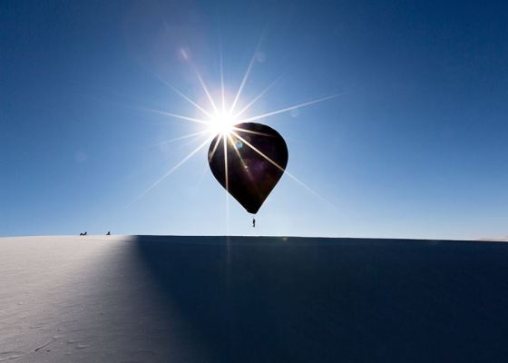 black balloon, person suspended, white desert, blue sky