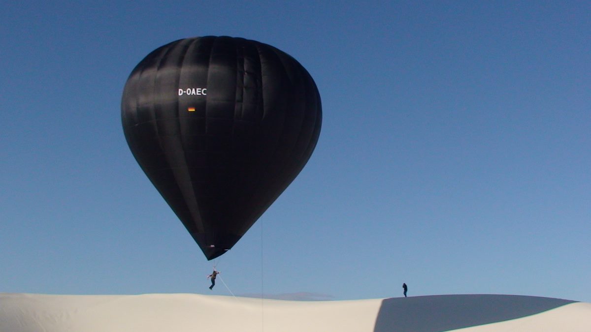 Black balloon, white desert, blue sky, person suspended